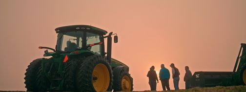 small group of farmers at sunrise next to tractor